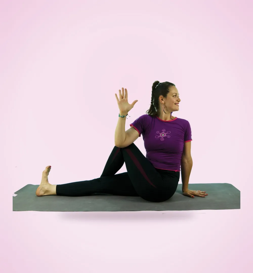 Tea într-o postură de yoga șezând, zâmbind și făcând cu mâna
